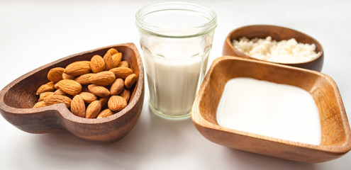 Homemade almond milk in a glass, almonds, milk and squeezed nut in wooden bowl on white background