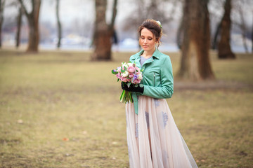Young beautiful girl in a long dress and a green jacket and with bouquet of flowers in her hands