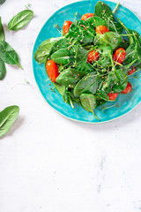 Salad of spinach, cherry tomatoes, sesame seeds and olive oil on a blue ceramic plate, top view, gray background. Vegetarian and vegan food, spring food.