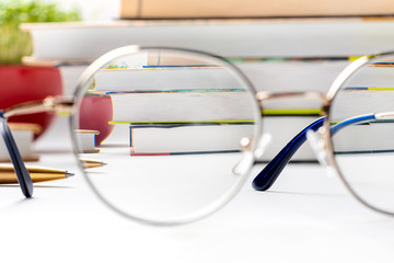 Look on books through eyeglasses lens, focus on books. Glasses and books lie on a white desktop....