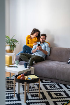 Happy couple stock photo. Smiling couple looking at mobile phone at home