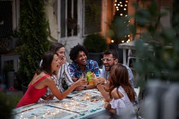 group of five adults making toast with cocktails, at the outdoor bar, laughing, having fun. Fun, party, socializing, multiethnic, introvert and extrovert persons concept