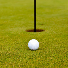 Golf ball on green with flag. Shallow depth of field. Focus on the ball.