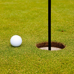 Golf ball on green with a hole. Shallow depth of field. Focus on the ball and the hole.