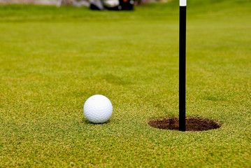 Golf ball on green with flag. Shallow depth of field. Focus on the ball and the flag.