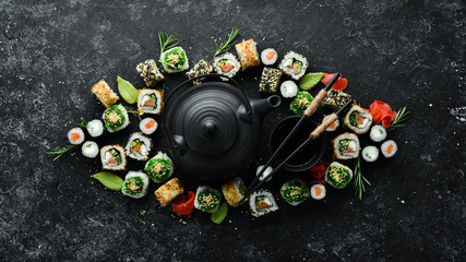 Sushi rolls and teapot with tea on black stone background. Great set of Japanese food