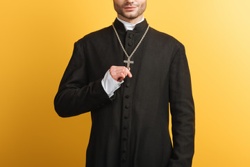 cropped view of catholic priest touching cross on his necklace isolated on yellow
