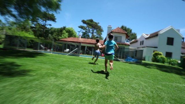 Kids running in backyard home garden and jumping splashing into pool water