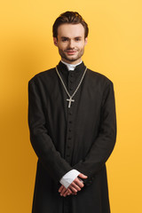 young catholic priest smiling at camera while standing isolated on yellow