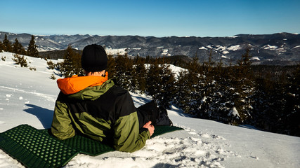 Fototapeta na wymiar guy lies and admires the mountain winter scenery