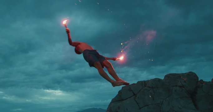 Extreme sports stunt man backflipping off of a sea cliff into the ocean with burning hot red flares, radical stuntman moments, people being awesome