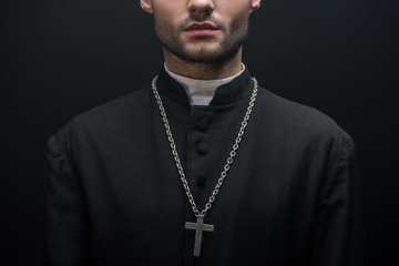 partial view of catholic priest with silver cross on necklace isolated on black