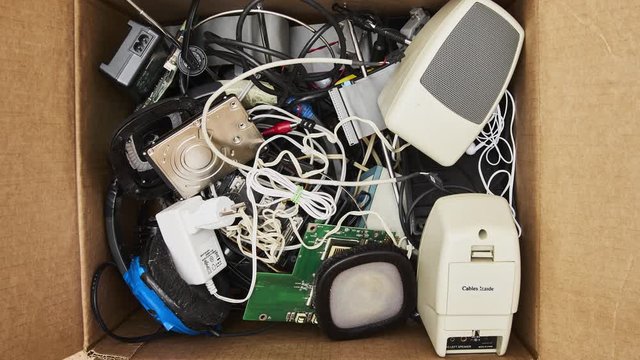 Modern electronic waste in a cardboard box. HDD, power supply, speaker, cable, headphone, antenna, computer parts, circuit board. 4K stop motion animation seamless loop