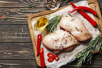 raw chicken fillet with rosemary, lemon, oil, pepper and other spices on a wooden background