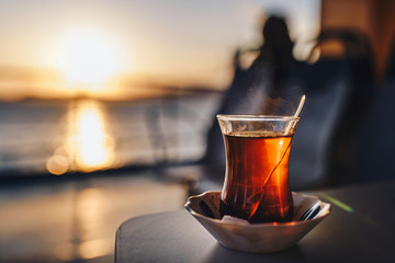 Obraz premium Hot black turkish tea on a table. Turkish tea against the setting sun and the sea. Turkish ferry.