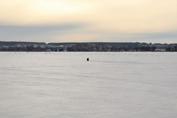 A frozen pond, snow, a fisherman, in the distance the city.