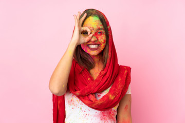 Young Indian woman with colorful holi powders on her face isolated on pink background showing ok sign with fingers
