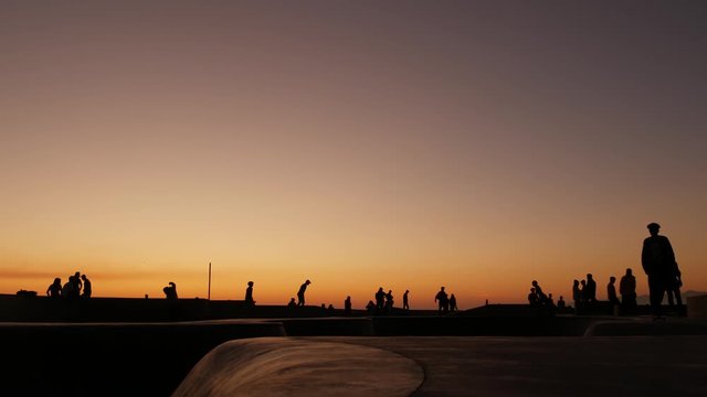 Silhouette of young jumping skateboarder riding longboard, summer sunset background. Venice Ocean Beach skatepark, Los Angeles California. Teens on skateboard ramp, extreme park. Group of teenagers