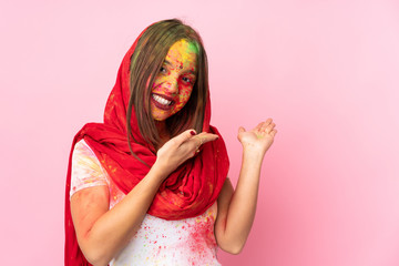 Young Indian woman with colorful holi powders on her face isolated on pink background extending hands to the side for inviting to come