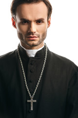 Young, concentrated catholic priest with silver cross on necklace looking at camera isolated on white