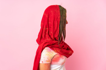 Young Indian woman with colorful holi powders on her face isolated on pink background in back position and looking back