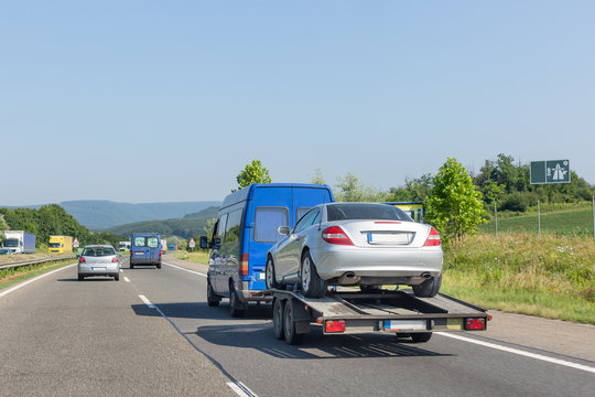 Car carrier trailer with car. Blue minibus with tow truck transporter carrying car on highway