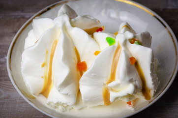 Close-up ice cream sundae with colored fruit slices on a white plate .