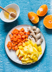 Ingredients for vitamin smoothies - fresh ripe mango, carrot, orange, honey, ginger on a blue background, top view. Detox healthy drink