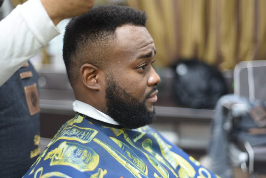 Black man in the Spanish barbershop. Cute black man makes a haircut in the African salon. Hair style. Haircut  for adults. 