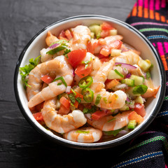 Mexican shrimp ceviche with tomato and serrano pepper on black background