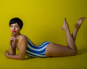Attractive brunette lies on her stomach in a striped bikini. Short-haired young woman in bodysuit...