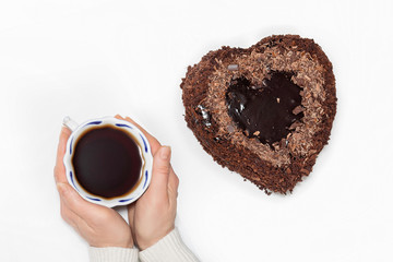 Hands with a cup of tea and a heart-shaped cake .