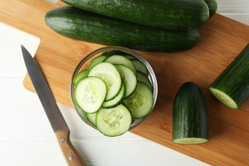 Board with cucumber and knife on wooden background, top view