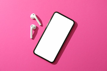 Phone with empty screen and headphones on pink background, top view