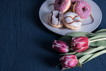 white and pink donuts and red tulips lie on a table