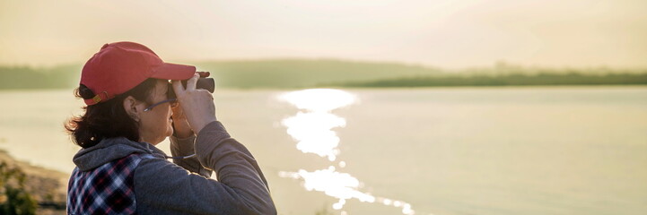 Woman looking through binoculars at summer sunny dawn.