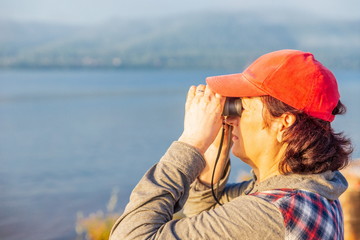 Woman looking through binoculars at summer sunny dawn.
