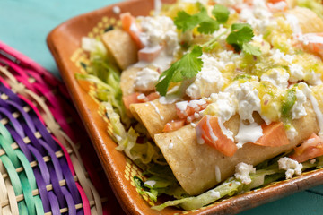 Mexican potato and cheese fried tacos also called flautas with green sauce on turquoise background