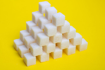Sugar cubes pyramid on a yellow background, creative food idea