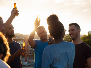 Happy people cheering with beer bottles against sunset. Relaxed young friends relaxing together in...