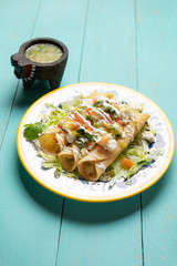 Mexican potato and cheese fried tacos also called flautas with green sauce on turquoise background