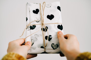 a gift in a woman's hand wrapped in homemade wrapping paper with black hearts tied with jute thread for Valentine's day