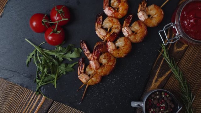 Grilled prawns on a skewer with cherry tomatoes and herbs lie on a metal plate. Fried shrimp on skewers with tomato sauce and spices