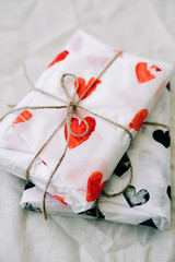 two gifts wrapped in homemade wrapping paper with red and black hearts tied with jute thread for Valentine's day on a white table