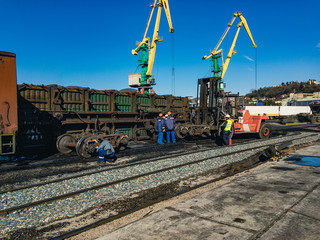 Fototapeta na wymiar Railway gondola that fell on its side. Workers liquidate the accident on a sunny day against the blue sky.