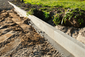 A sidewalk is under construction, a concrete curb is being installed and the foundation of the road is being prepared.