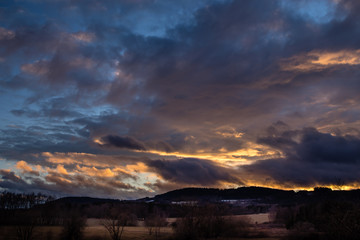 Beautiful sunset - red sky over hilly landscape, blue sky with orange-colored clouds