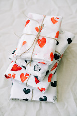 a stack of gifts wrapped in homemade wrapping paper with red and black hearts tied with jute thread for Valentine's day on a white table