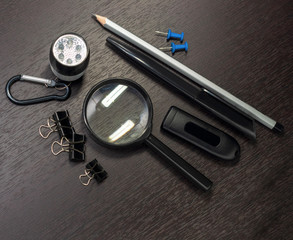 Chancery on a wooden table, magnifier, pen, pencil, binders clip, paper clip, flashlight, flash drive and buttons. Set of detective. Desk. Dark photo.Selective focus.