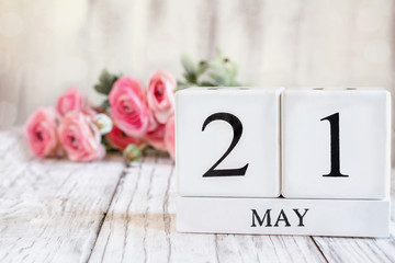 White wood calendar blocks with the date May 21st. Selective focus with pink ranunculus in the background over a wooden table.